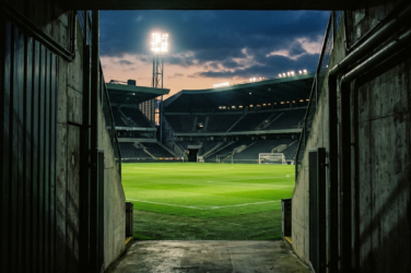 Empty floodlit football stadium viewed from a dark tunnel