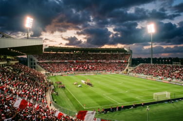 Packed football stadium with players gathered on a brightly lit field