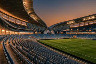 Empty modern football stadium with illuminated roof and green pitch at dusk
