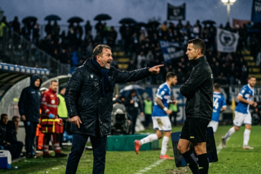 Coach pointing while speaking with match official during a rainy football match